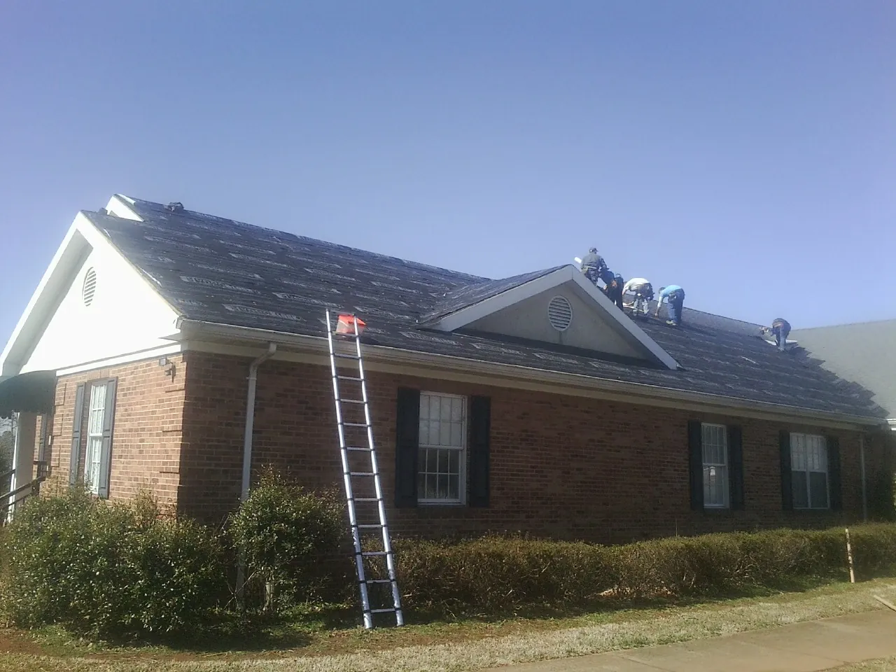 Crew tearing shingles off a brick ranch roof with a ladder set — Metal Roof Repair work by our crew in Lafayette Hill