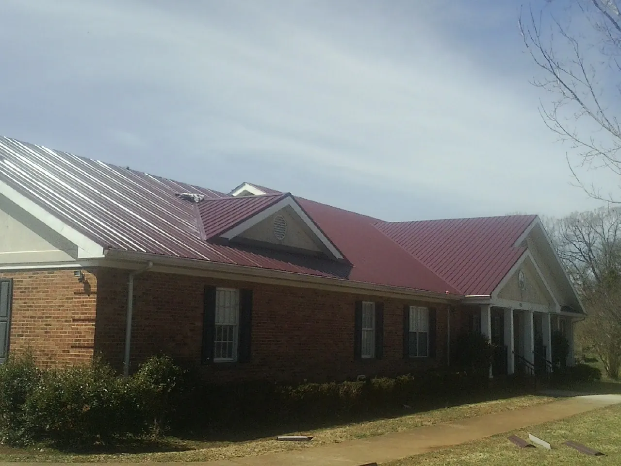 Red metal roof with gabled entries on a long brick building, from a Hail Damage Roof Repair job in Lafayette Hill