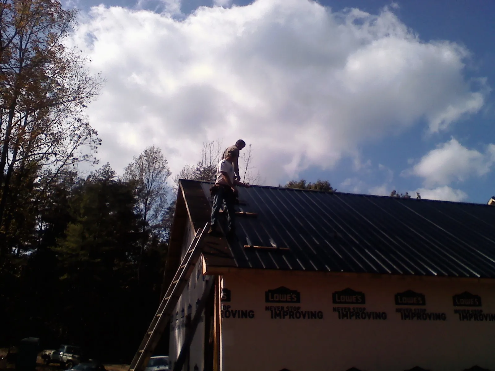 Roofer fastening dark metal panels high against a cloudy sky, from a Roof Inspection job in Lafayette Hill