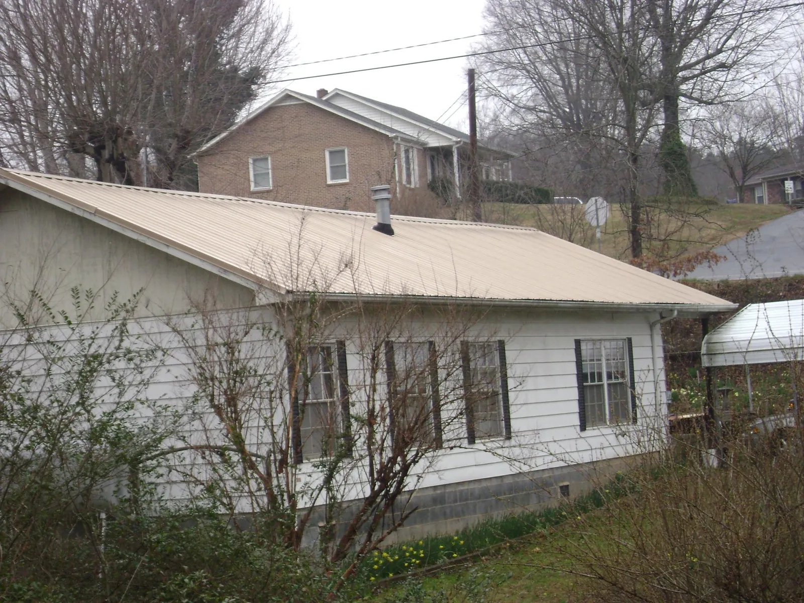 Tan metal roof on a white sided house set into a hillside — Commercial Roofing by Roofing Brothers in Lafayette Hill