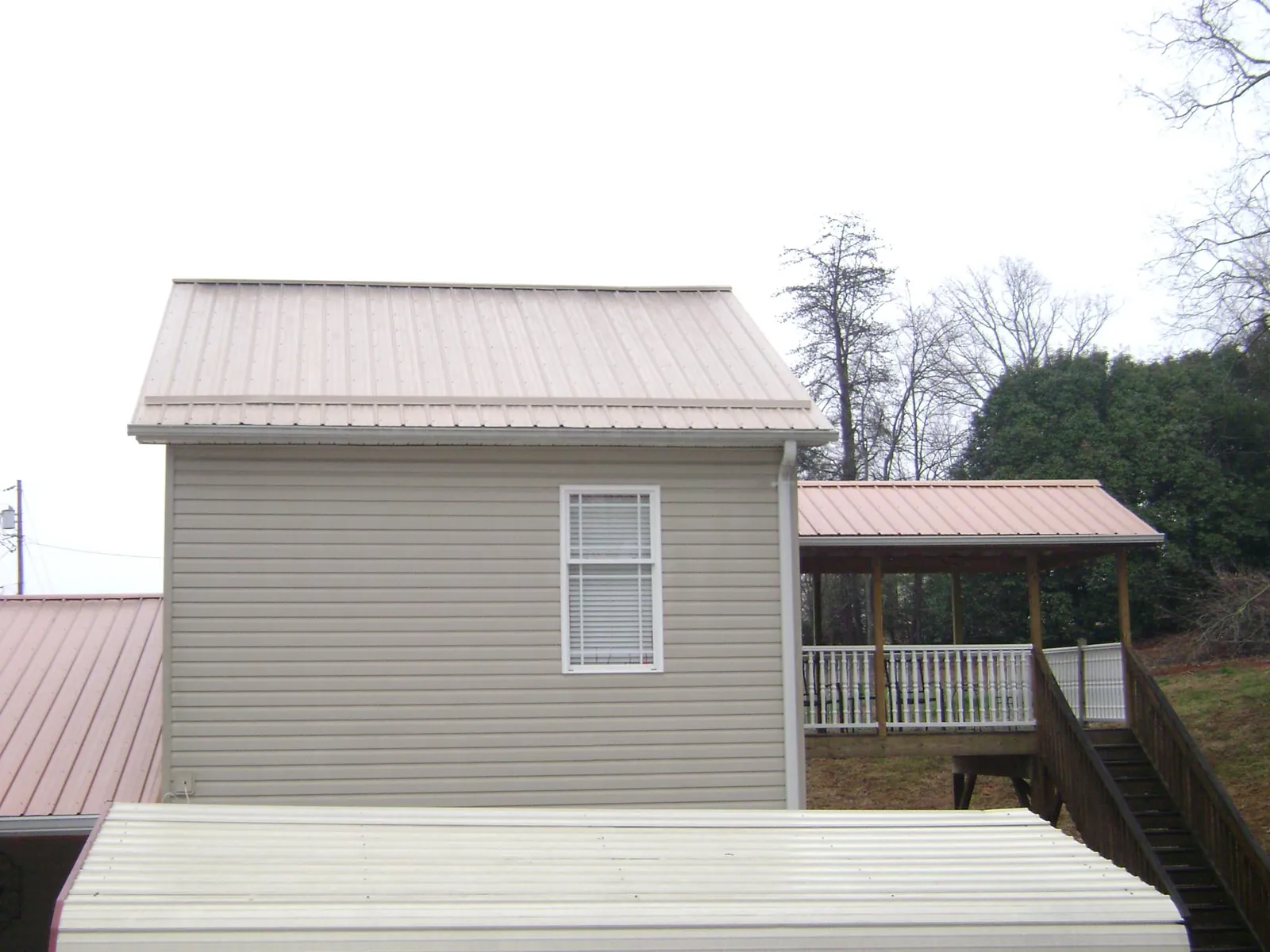 Tan metal roofs on a two story addition and attached porch, from a Roof Replacement job in Lafayette Hill